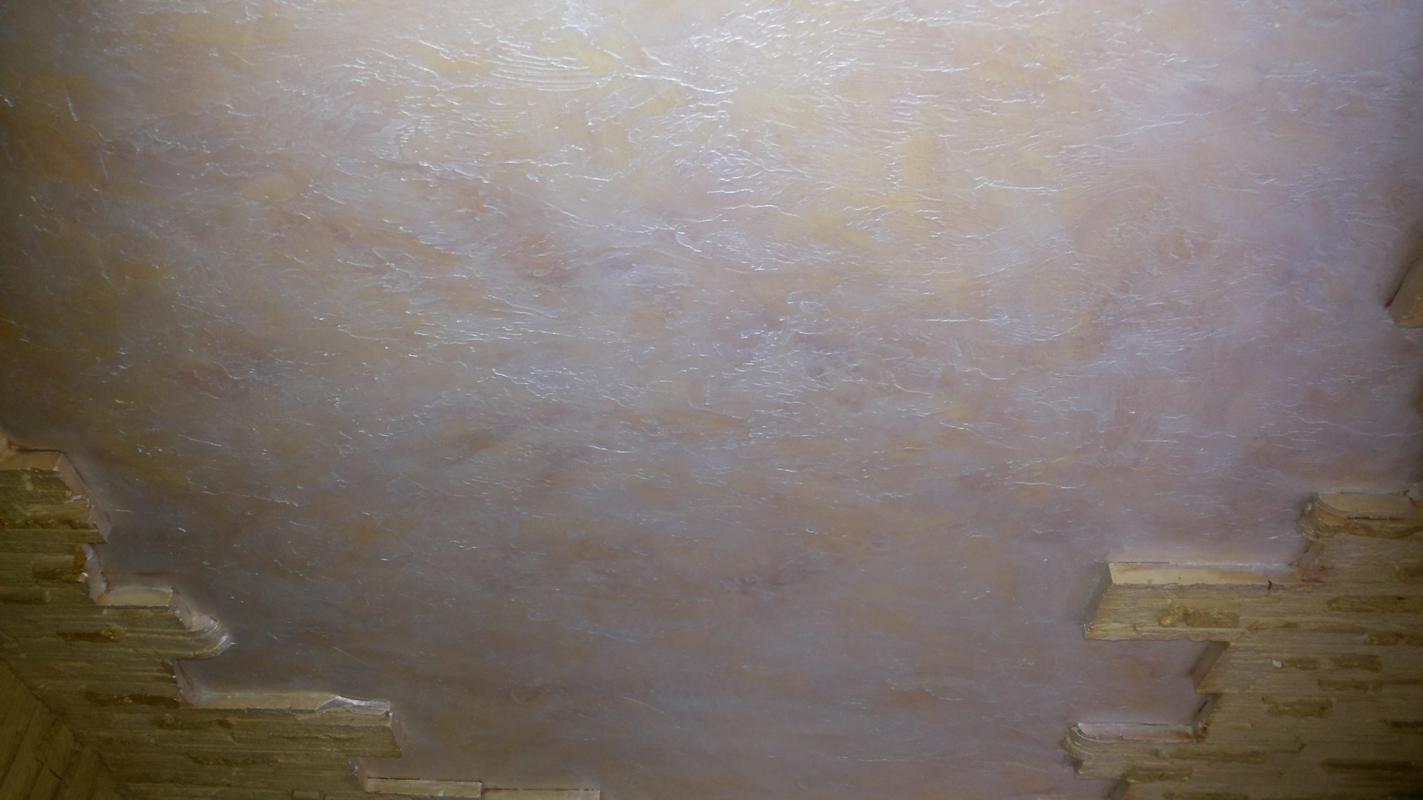 Beżowy sufit z dekoracyjną fakturą i fragmentem ozdobnego wykończenia ściany z cegieł w rogu.