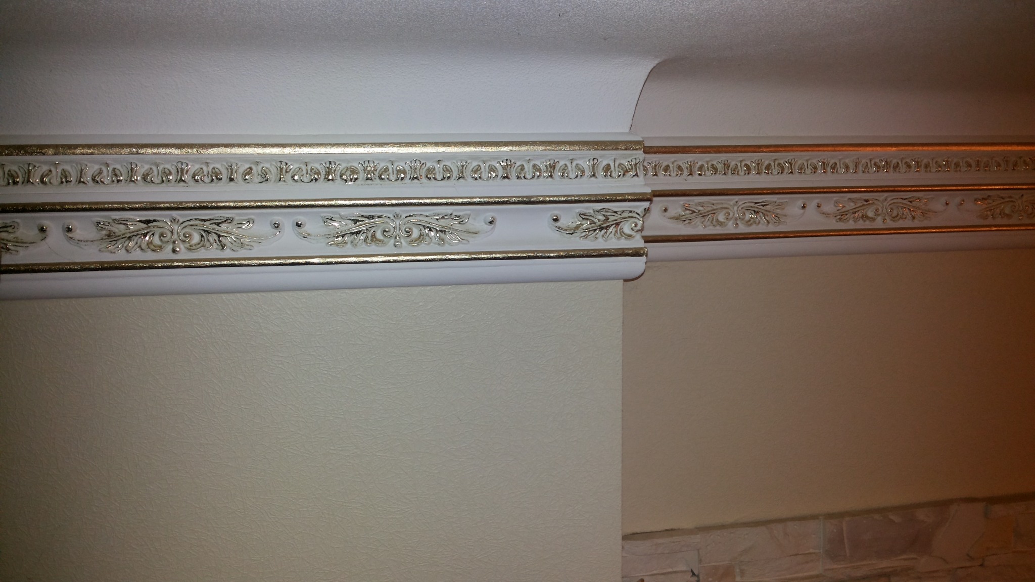 Dekoracyjna listwa przysufitowa z ornamentami w kolorze białym i złotym, zamontowana na styku ściany i sufitu w jasnym pomieszczeniu.