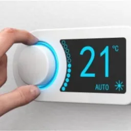 Dłoń ustawia temperaturę na nowoczesnym termostacie ściennym z podświetlanym wyświetlaczem wskazującym 21 stopni Celsjusza.