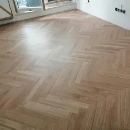 Ukończona podłoga z paneli ułożonych w jodełkę w mieszkaniu w Warszawie Praga, widoczne gniazdka elektryczne na ścianie.