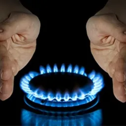 Płomień palnika gazowego otoczony dłońmi na czarnym tle, symbolizujący kontrolę i bezpieczeństwo użytkowania gazu.