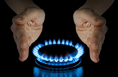 Płomień palnika gazowego otoczony dłońmi na czarnym tle, symbolizujący kontrolę i bezpieczeństwo użytkowania gazu.