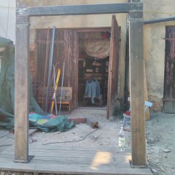 Marcin Birski - Metalowa konstrukcja spawana we Wrocławiu, prawdopodobnie pergola lub altana, w trakcie montażu na drewnianym podeście, z widocznymi śladami spawania i otwartymi drzwiami warsztatu w tle.