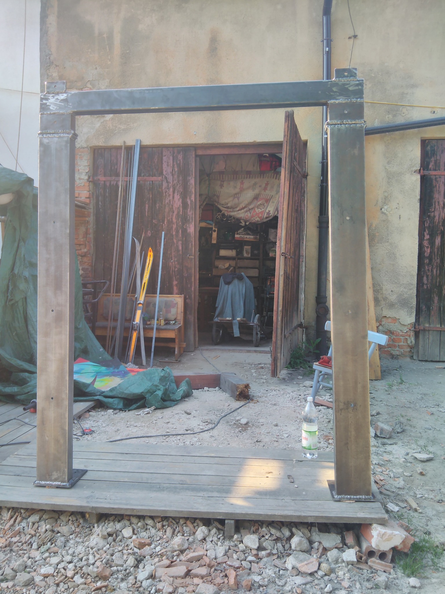 Metalowa konstrukcja spawana we Wrocławiu, prawdopodobnie pergola lub altana, w trakcie montażu na drewnianym podeście, z widocznymi śladami spawania i otwartymi drzwiami warsztatu w tle.