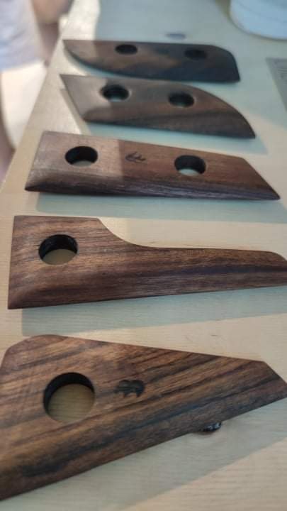 Ręcznie wykonane, drewniane narzędzia do obróbki gliny z okrągłymi otworami, ułożone w rzędzie na jasnym blacie. Na jednym z narzędzi widoczne małe logo w kształcie zwierzęcia.