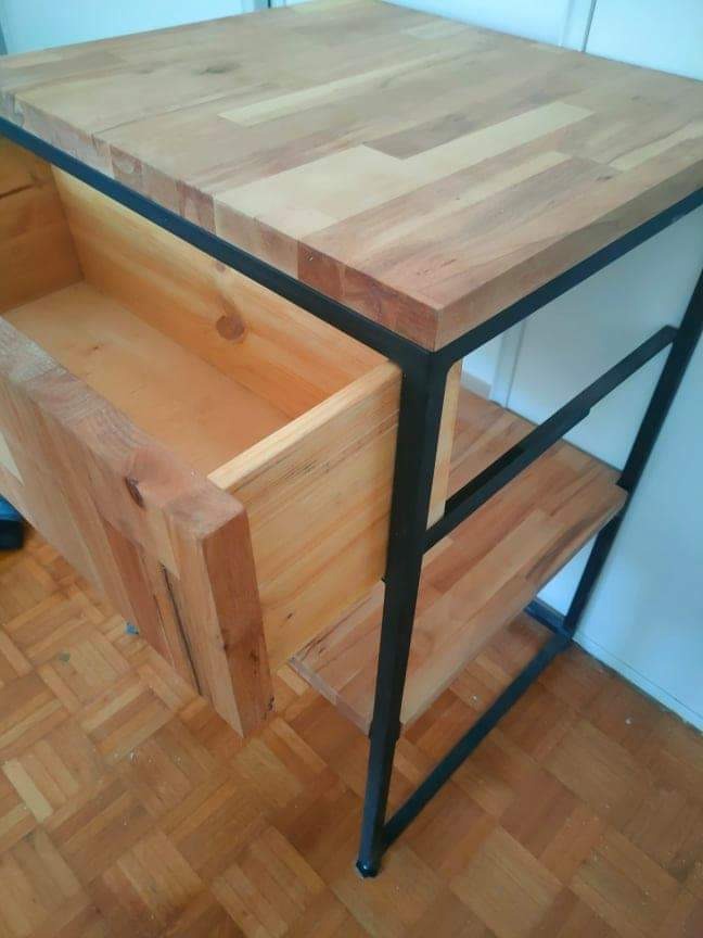 Stolik drewniany z wysuwaną szufladą i metalową ramą, widoczny na tle parkietu.