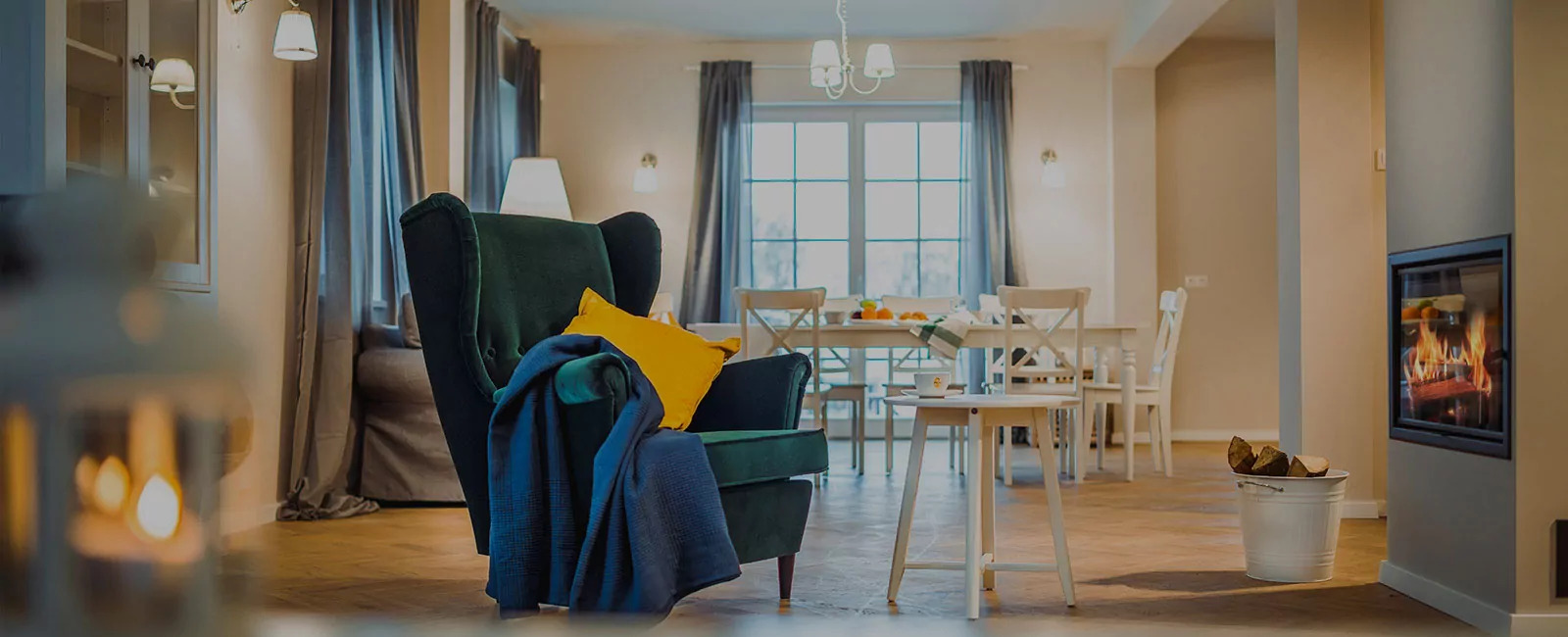 Jasne wnętrze salonu z zielonym fotelem, żółtą poduszką, niebieskim pledem i kominkiem w tle, drewniana podłoga i białe meble.