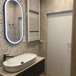 Foremen Sp. z o.o. - Nowoczesna łazienka z owalną umywalką nablatową, czarną armaturą, podświetlanym lustrem i grzejnikiem drabinkowym na ścianie z mozaiką.