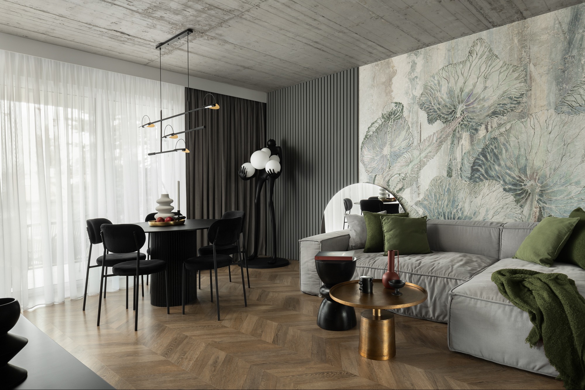 Nowoczesne wnętrze z betonowym sufitem, drewnianą podłogą ułożoną w jodełkę, ścianą z tapetą w motywy roślinne i czarnymi krzesłami przy okrągłym stole.