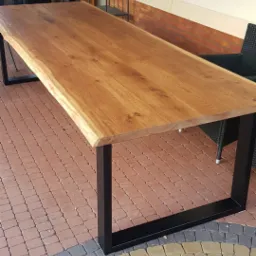 St&oacute;ł z blatem z litego drewna dębowego o nieregularnej krawędzi, wsparty na czarnych, metalowych nogach o kwadratowym przekroju, ustawiony na ceglanym patio.
