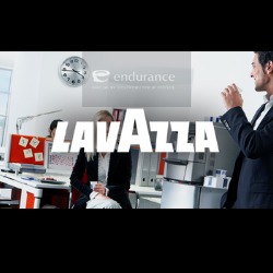 Biuro z pracownikami, ekspres do kawy w tle, logo Lavazza na pierwszym planie, zegar na ścianie i logo firmy Endurance. Mężczyzna w garniturze pije kawę z białego kubka.