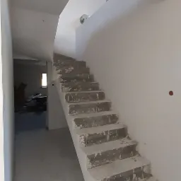 Surowe betonowe schody w trakcie wykańczania w nowym budynku, widoczne nierówności i niedoskonałości powierzchni przed finalnym wykończeniem.