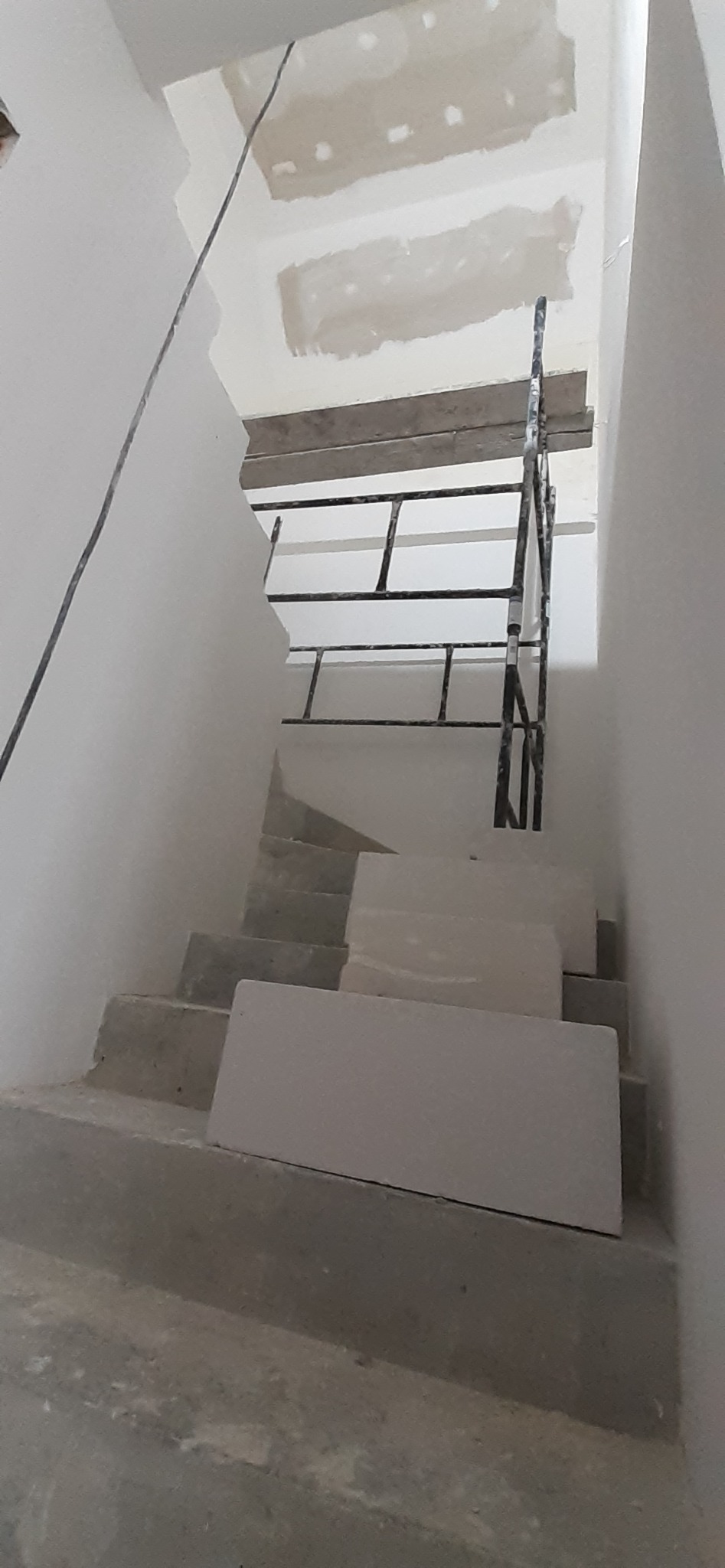 Wnętrze w trakcie prac wykończeniowych: surowe schody betonowe z blokami z białego gazobetonu, fragment rusztowania i niedokończone fragmenty sufitu z widocznymi śladami po szpachlowaniu.