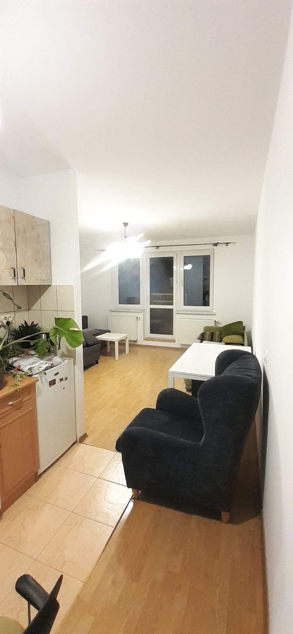 Jasne wnętrze pokoju z aneksem kuchennym, świeżo odmalowane ściany i sufit, widoczne meble i podłoga po remoncie.