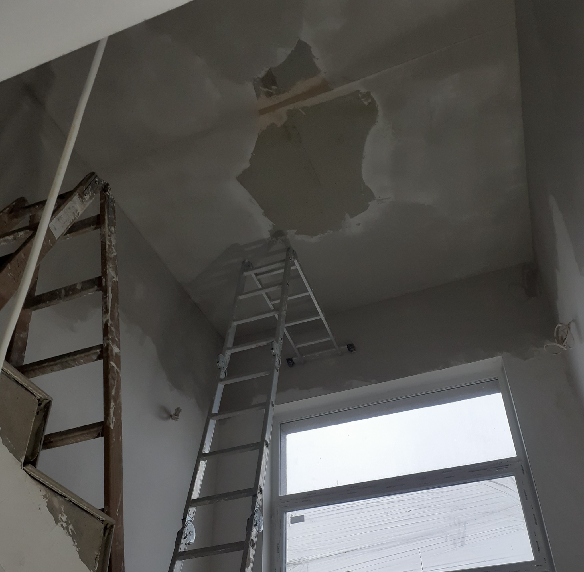 Wnętrze w trakcie prac wykończeniowych; widoczne dwie drabiny, fragment okna i sufit z widocznym miejscem po łataniu ubytku.