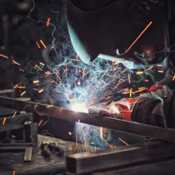 Spawacz w masce spawalniczej łączy metalowe profile, iskry i dym w warsztacie.