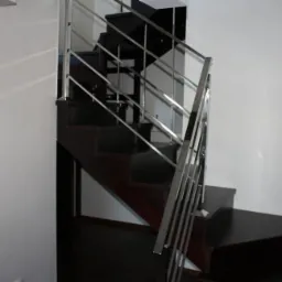 Ciemne drewniane schody z metalową balustradą w jasnym wnętrzu, widoczne z dołu.