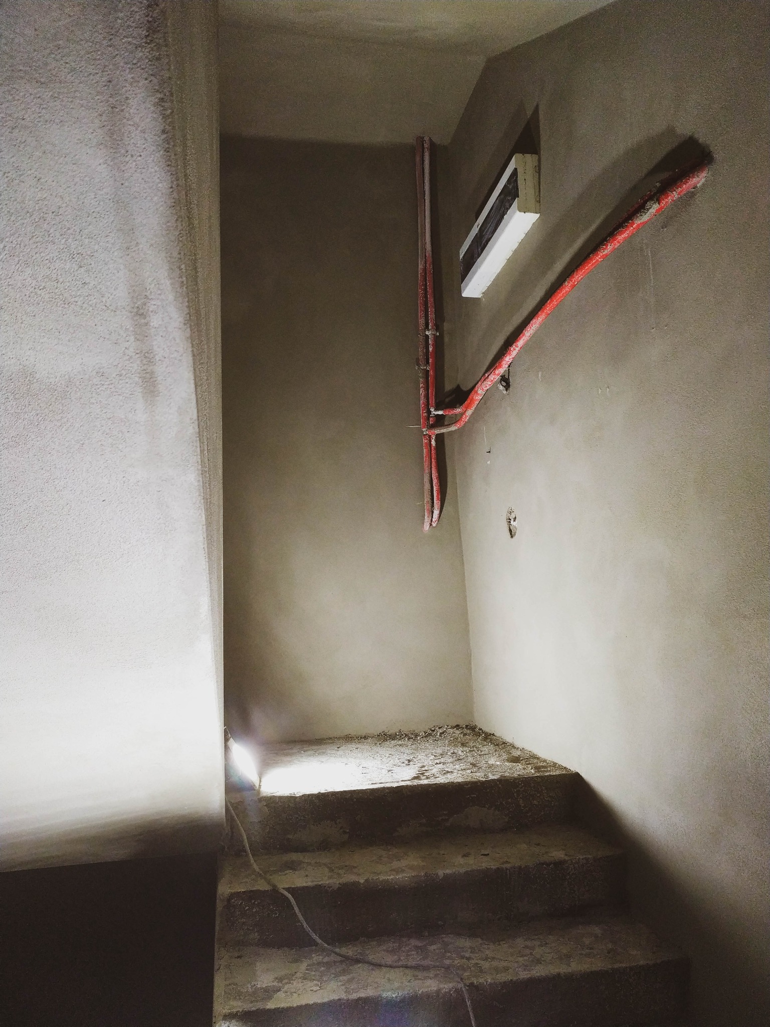 Świeżo położone tynki maszynowe na ścianach klatki schodowej w Lublinie, z widocznymi przewodami elektrycznymi i niedokończonymi schodami.