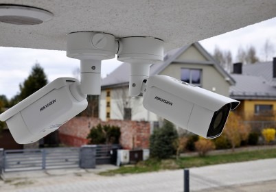 Trzy białe kamery Hikvision zamontowane pod sufitem z widokiem na dom i ogrodzenie.