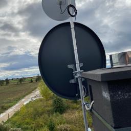 Getmon - Dwie anteny satelitarne zamontowane na metalowym maszcie, widoczne przewody, tło to pochmurne niebo i krajobraz wiejski z polami i lasami.