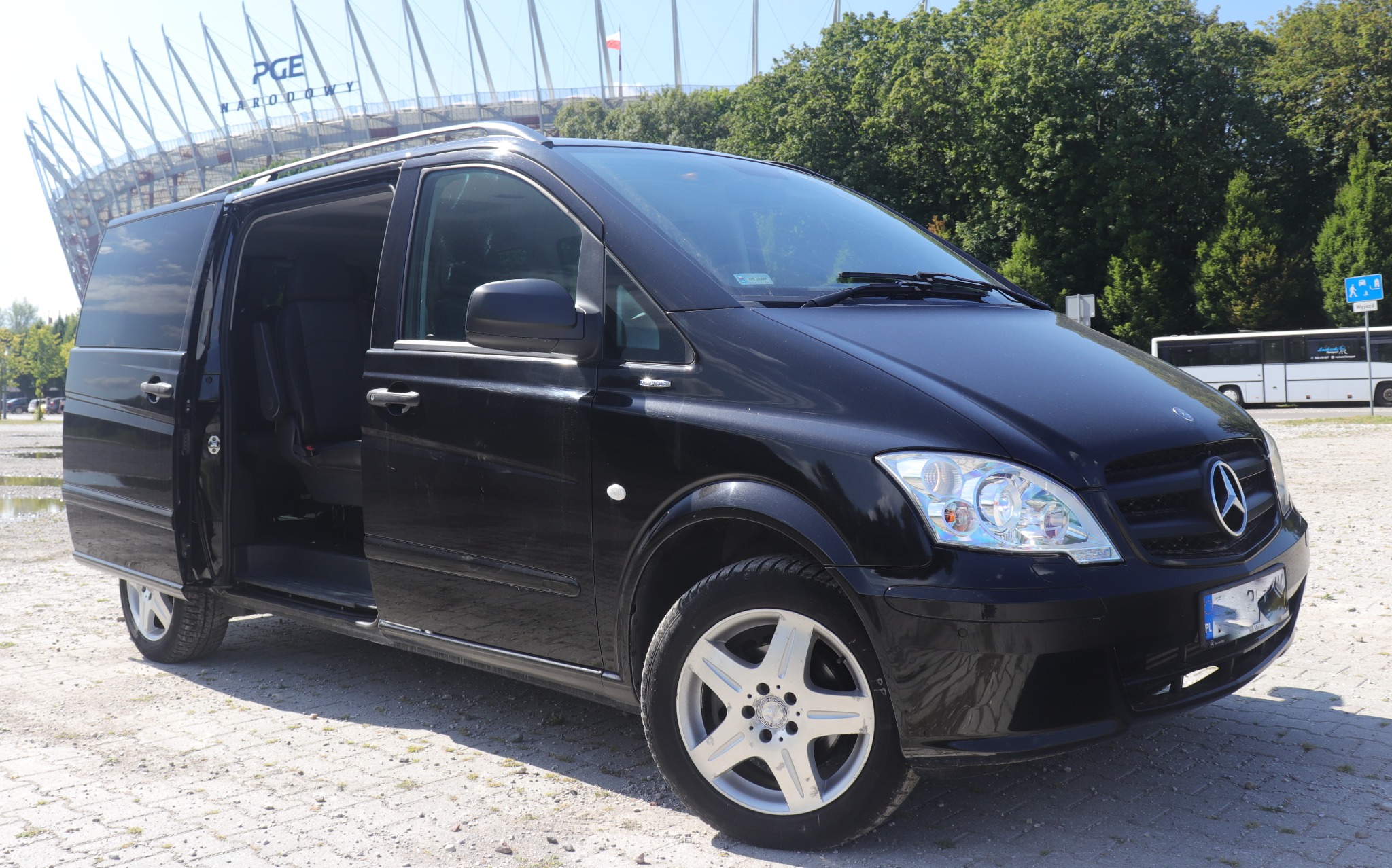 Czarny Mercedes Vito z otwartymi drzwiami przesuwnymi na tle Stadionu Narodowego w słoneczny dzień.