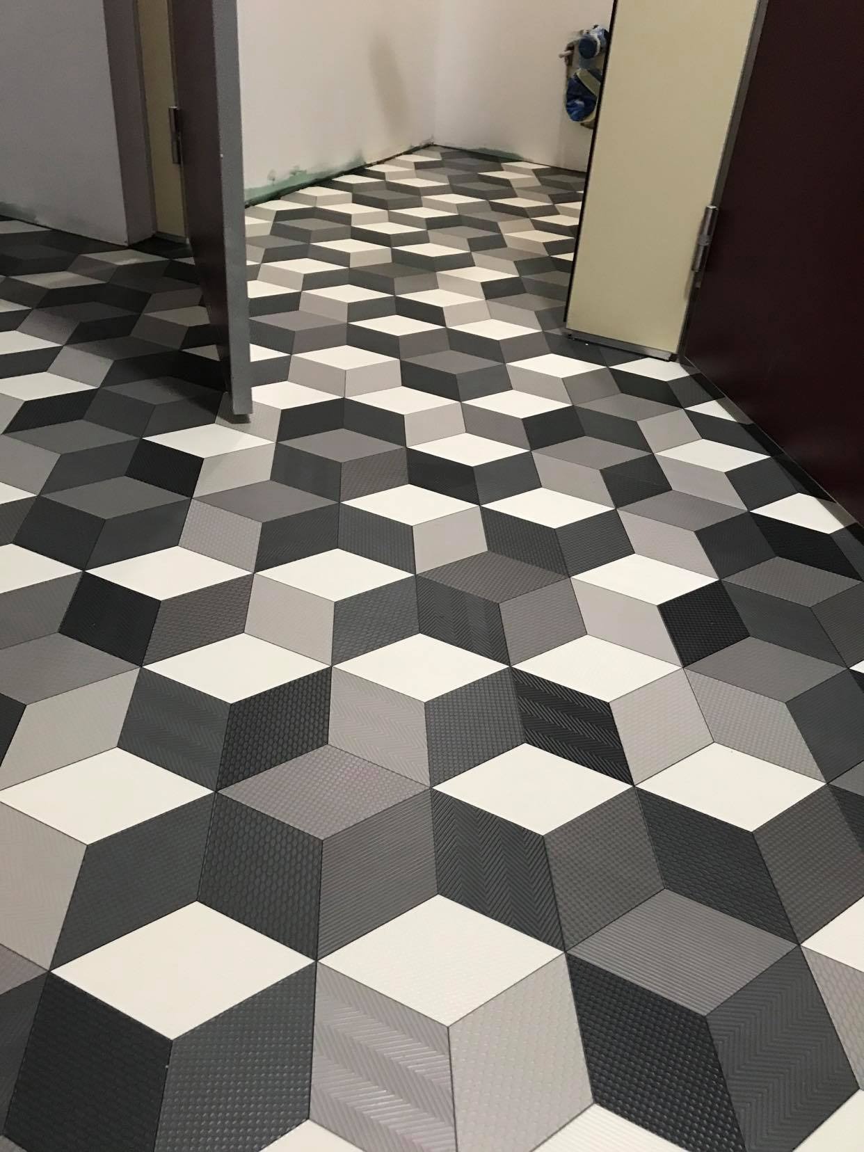 Podłoga wyłożona panelami lub płytkami w geometryczny wzór 3D, imitującym kostki w odcieniach szarości i bieli, widok na fragment pomieszczenia z otwartymi drzwiami.