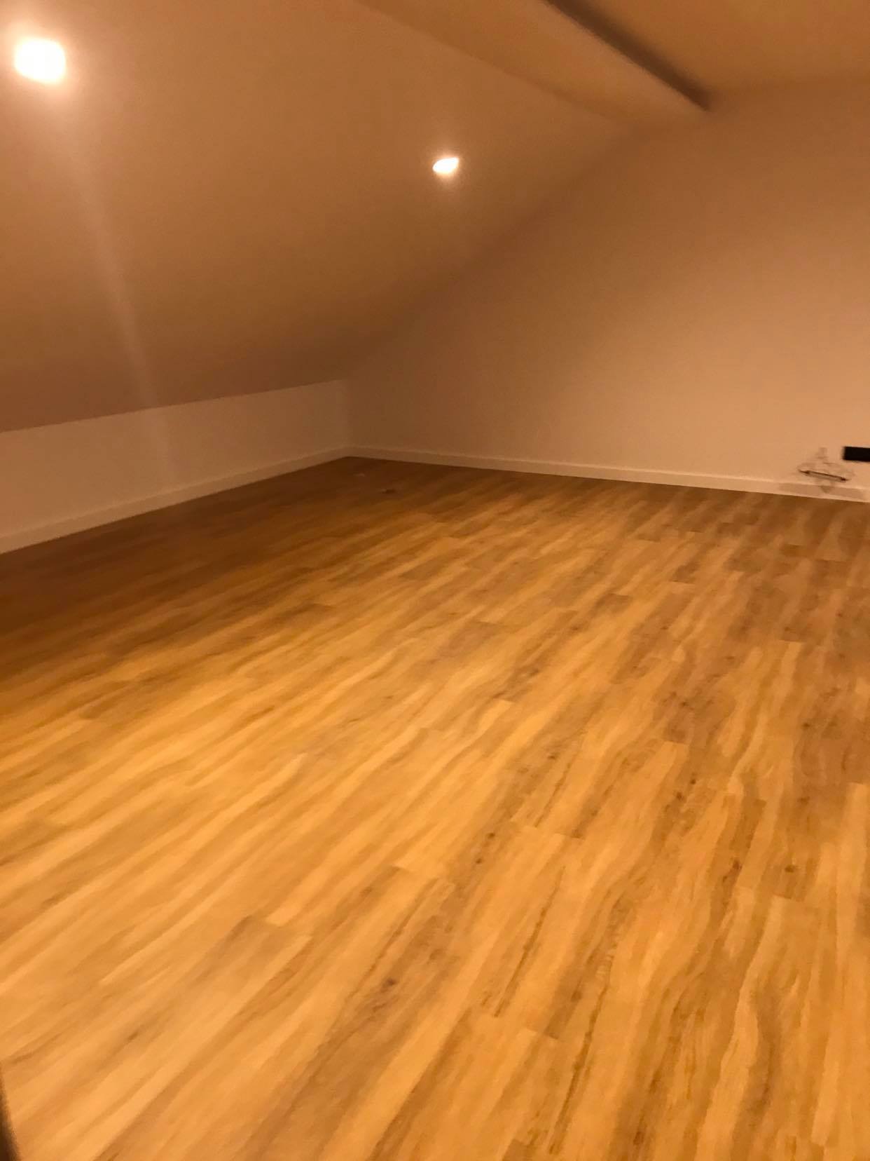 Nowo ułożone panele podłogowe w pustym pokoju na poddaszu, widoczne białe listwy przypodłogowe i punktowe oświetlenie sufitowe.