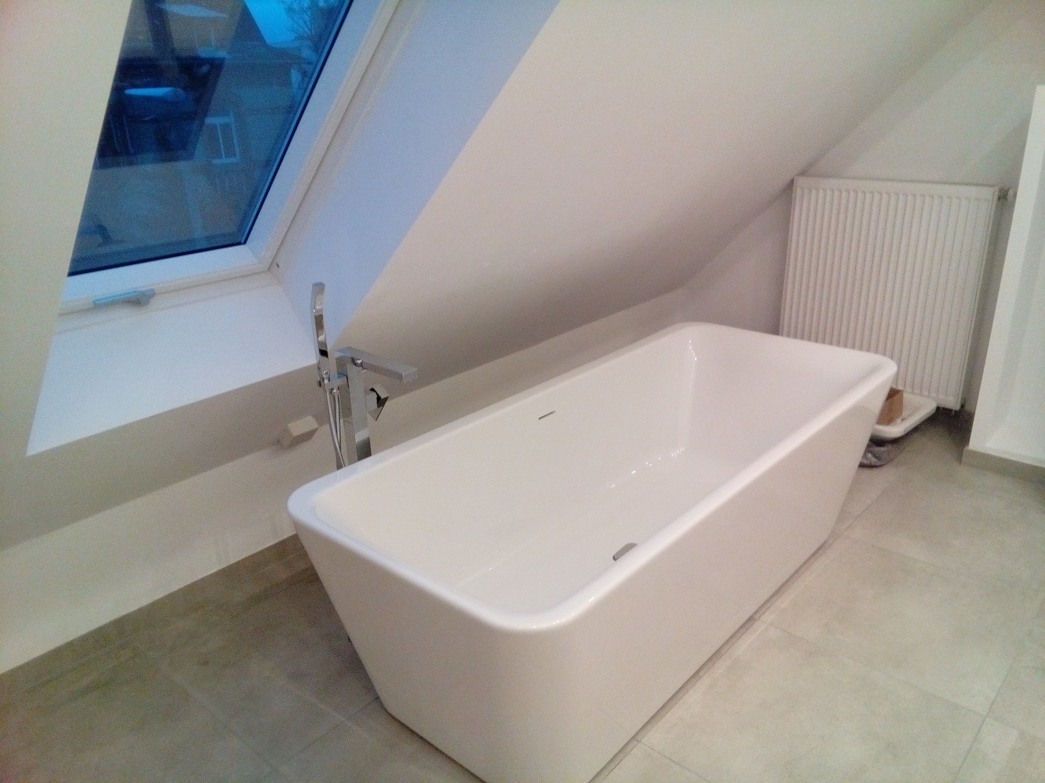 Nowoczesna, wolnostojąca wanna w łazience na poddaszu z oknem dachowym i grzejnikiem.