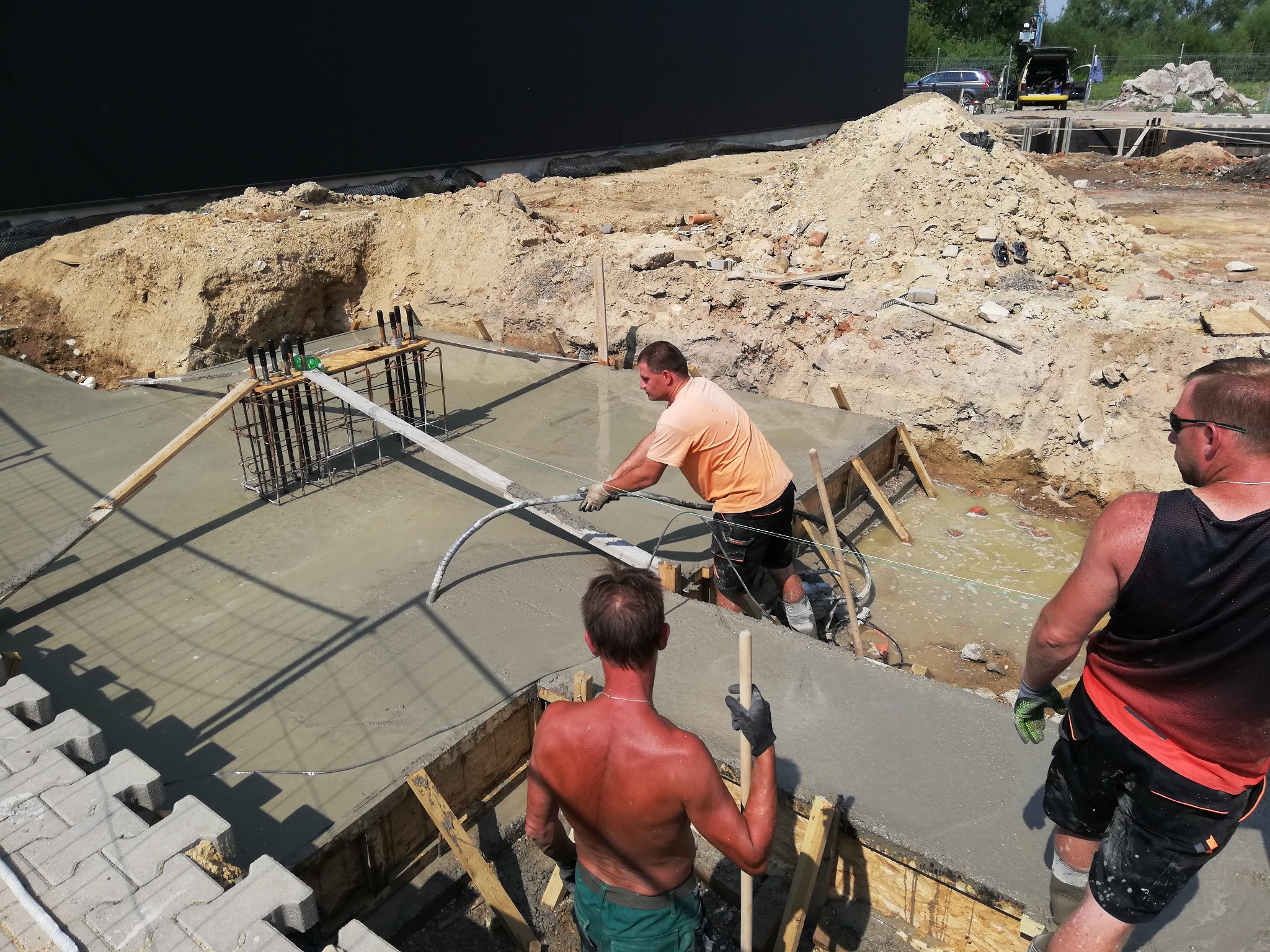 Wylewanie betonowego fundamentu pod budynek; pracownicy w trakcie rozprowadzania betonu i poziomowania powierzchni, widoczne szalunki i zbrojenie.