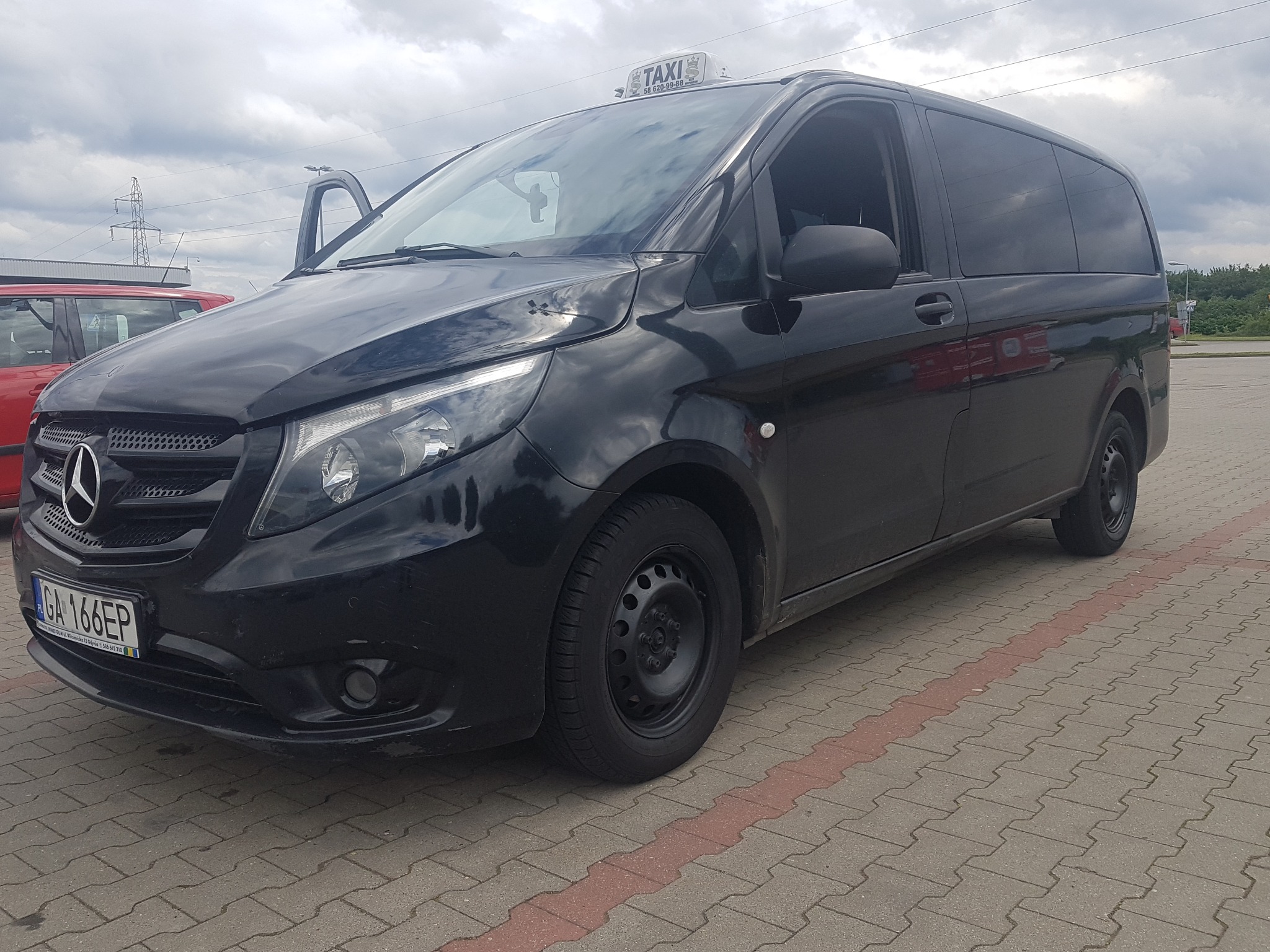 Czarny van Mercedes-Benz Vito Taxi z otwartymi drzwiami kierowcy, zaparkowany na brukowanym placu w Gdańsku. Tablica rejestracyjna widoczna.