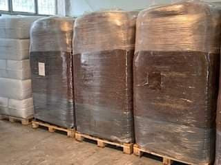 Palety z zapakowaną ziemią ogrodową w przezroczystej folii, widoczne etykiety na workach, ustawione w magazynie.