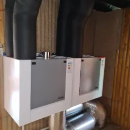 Zamontowany rekuperator Vasco z czarnymi rurami wentylacyjnymi w pomieszczeniu wykończonym boazerią.