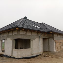 Usługi dekarsko-ciesielskie Ireneusz Rożek - Surowy stan domu jednorodzinnego z czarnym dachem z dachówki ceramicznej, widoczne okna dachowe i rynny. Dom w trakcie budowy, ściany z białego bloczka.