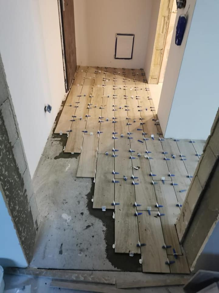 Układanie podłogi z płytek imitujących drewno z użyciem niebieskich krzyżyków dystansowych, widoczny fragment surowej podłogi przed położeniem płytek.