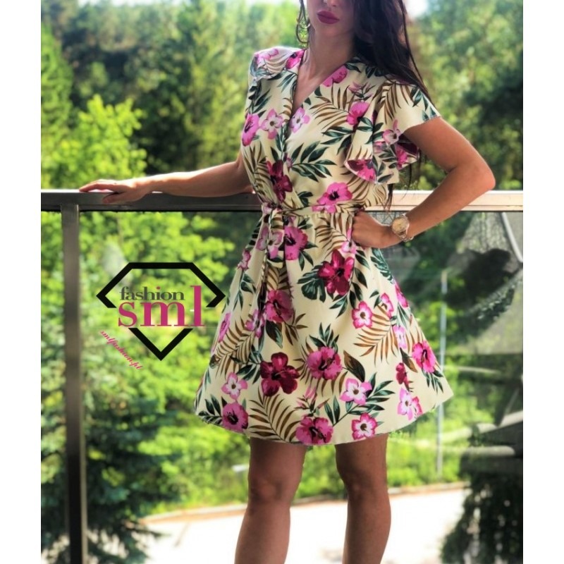 Kobieta prezentuje letnią sukienkę w kwiaty z krótkim rękawem na balkonie z widokiem na zieleń, z widocznym logo firmy na sukience.