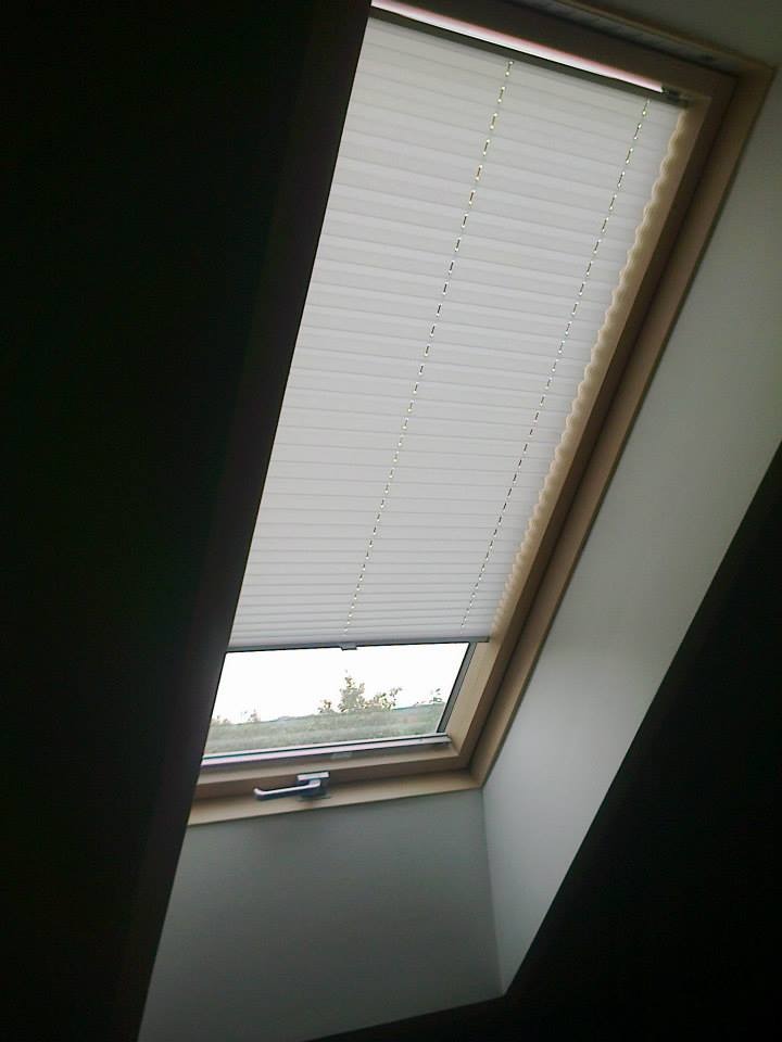 Zasłonięte okno dachowe z delikatną, białą osłoną przeciwsłoneczną w harmonijkę, widok z dołu.