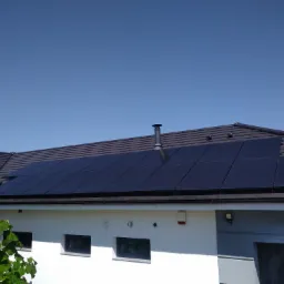 Ciemne panele słoneczne na dachu nowoczesnego domu z brązową dachówką, widok z dołu w słoneczny dzień.