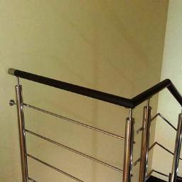 Inox 4 home - Wewnętrzna balustrada ze stali nierdzewnej z czarnym poręczą, widok z dołu schodów, grzejnik w tle.