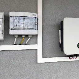 Dwa rozdzielacze elektryczne Hager i ETI oraz falownik Sofar zamontowane na szarej ścianie, połączone białymi listwami maskującymi.