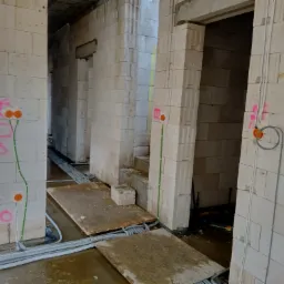 Wnętrze budynku w trakcie budowy z widocznymi przewodami elektrycznymi prowadzonymi w ścianach z betonu komórkowego, oznaczenia tras kablowych farbą, oraz peszle ułożone na podłodze.