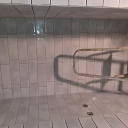 Świeżo ułożone, pionowe, białe płytki w kształcie cegiełek, z widoczną, metalową drabinką na tle, oraz dwoma okrągłymi odpływami w podłodze.