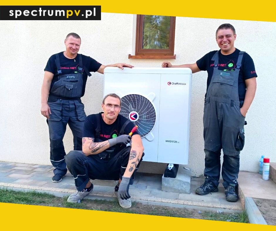 Trzech instalatorów w kombinezonach roboczych pozuje przy białej pompie ciepła Chaffoteaux Inverter, jeden z nich trzyma śrubokręt, widoczny fragment budynku z oknem i logo firmy spectrumpv.pl...