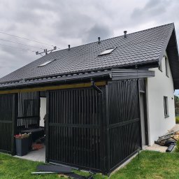 MAR-DACH Mariusz Boruc - Nowoczesny dom z czarnym dachem i ażurową, drewnianą konstrukcją. Widoczne elementy wykończeniowe i narzędzia sugerują trwające prace.