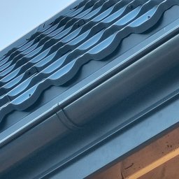 MAR-DACH Mariusz Boruc - Nowe, grafitowe pokrycie dachowe z blachy trapezowej, widoczne z dołu pod kątem. Zamontowana rynna i drewniana konstrukcja dachu.