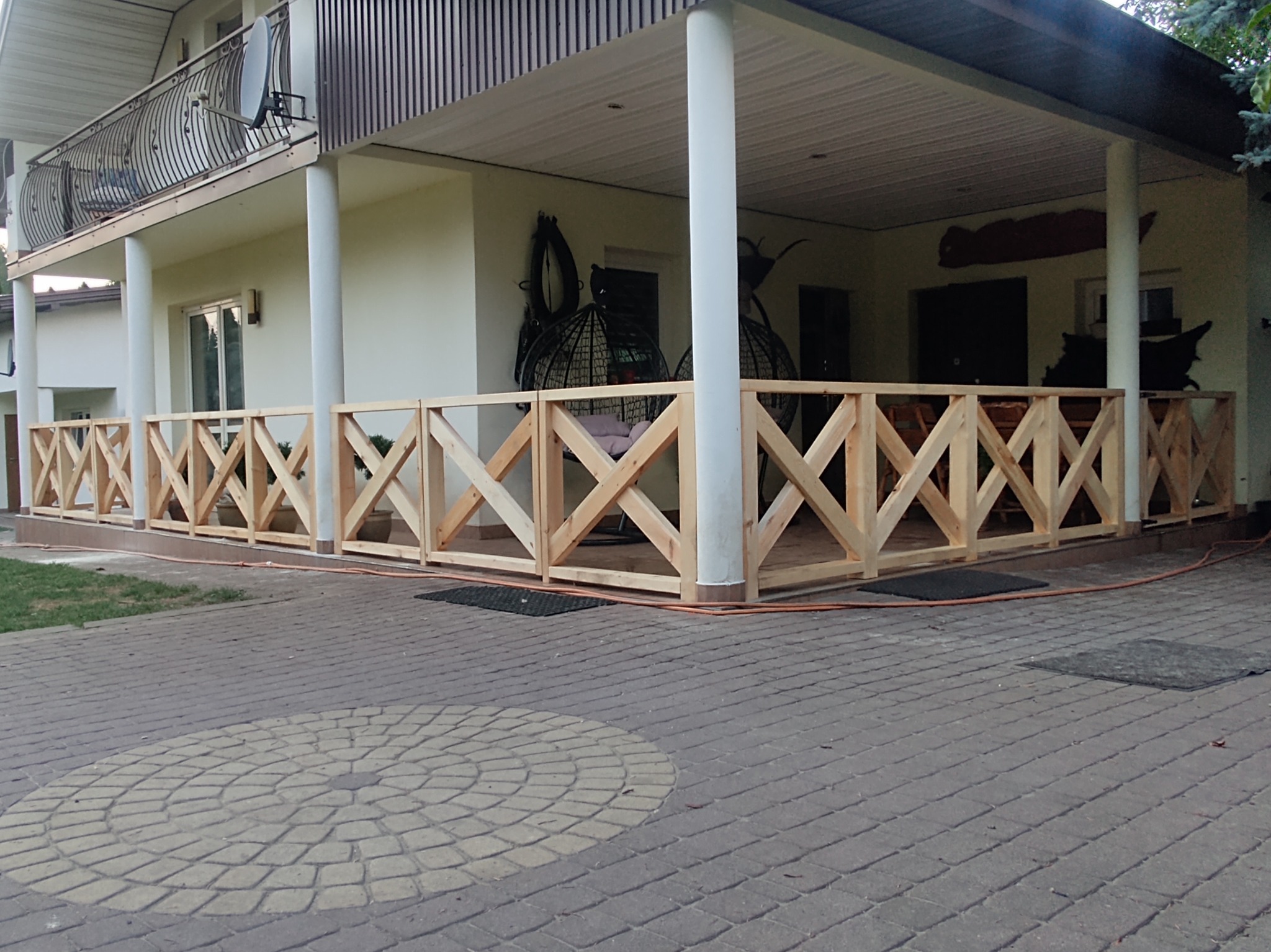 Nowoczesna balustrada z surowego drewna, zdobiąca taras domu z kolumnami. Widoczne detale konstrukcji i otoczenie budynku.