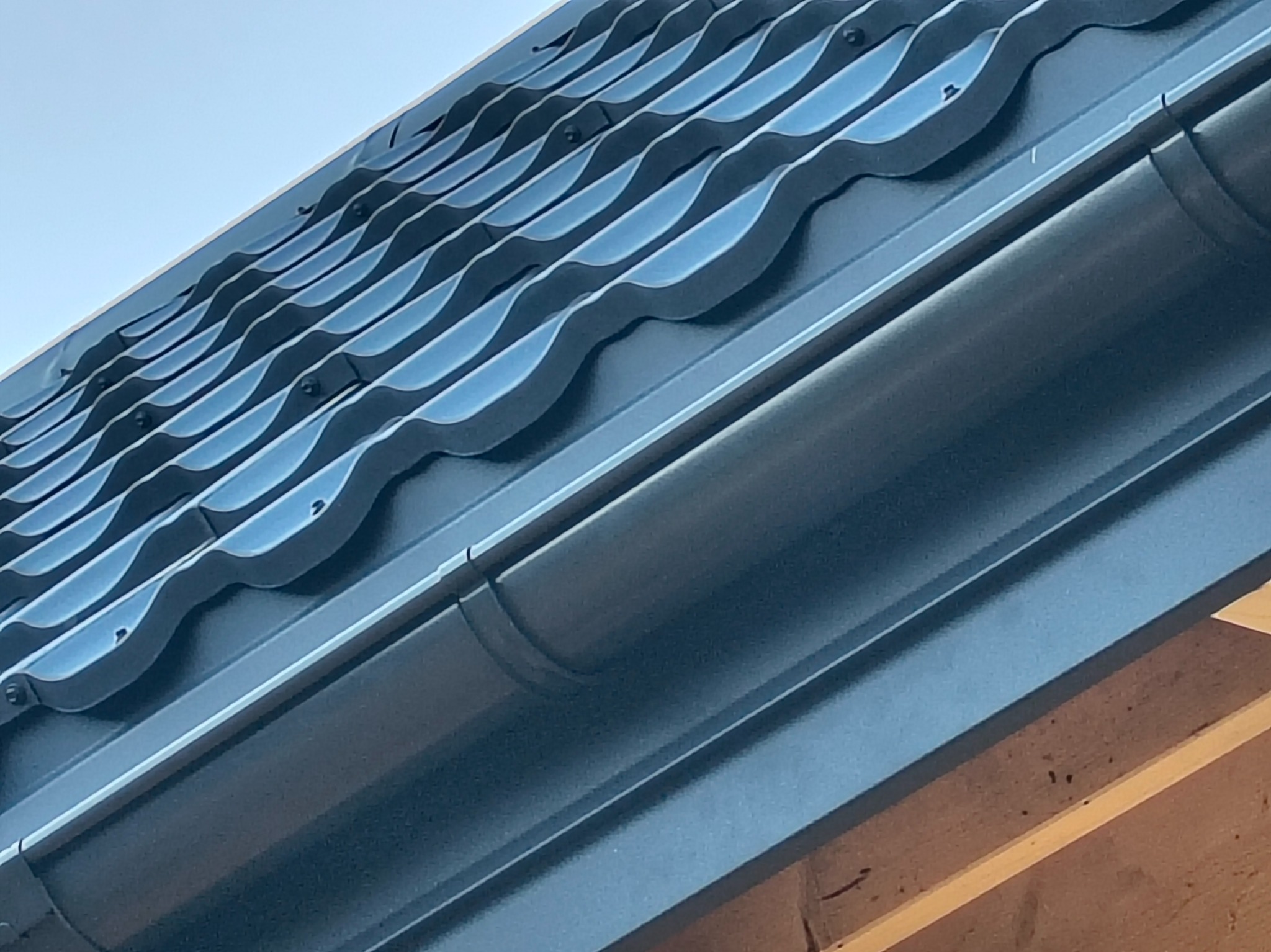 Nowe, grafitowe pokrycie dachowe z blachy trapezowej, widoczne z dołu pod kątem. Zamontowana rynna i drewniana konstrukcja dachu.