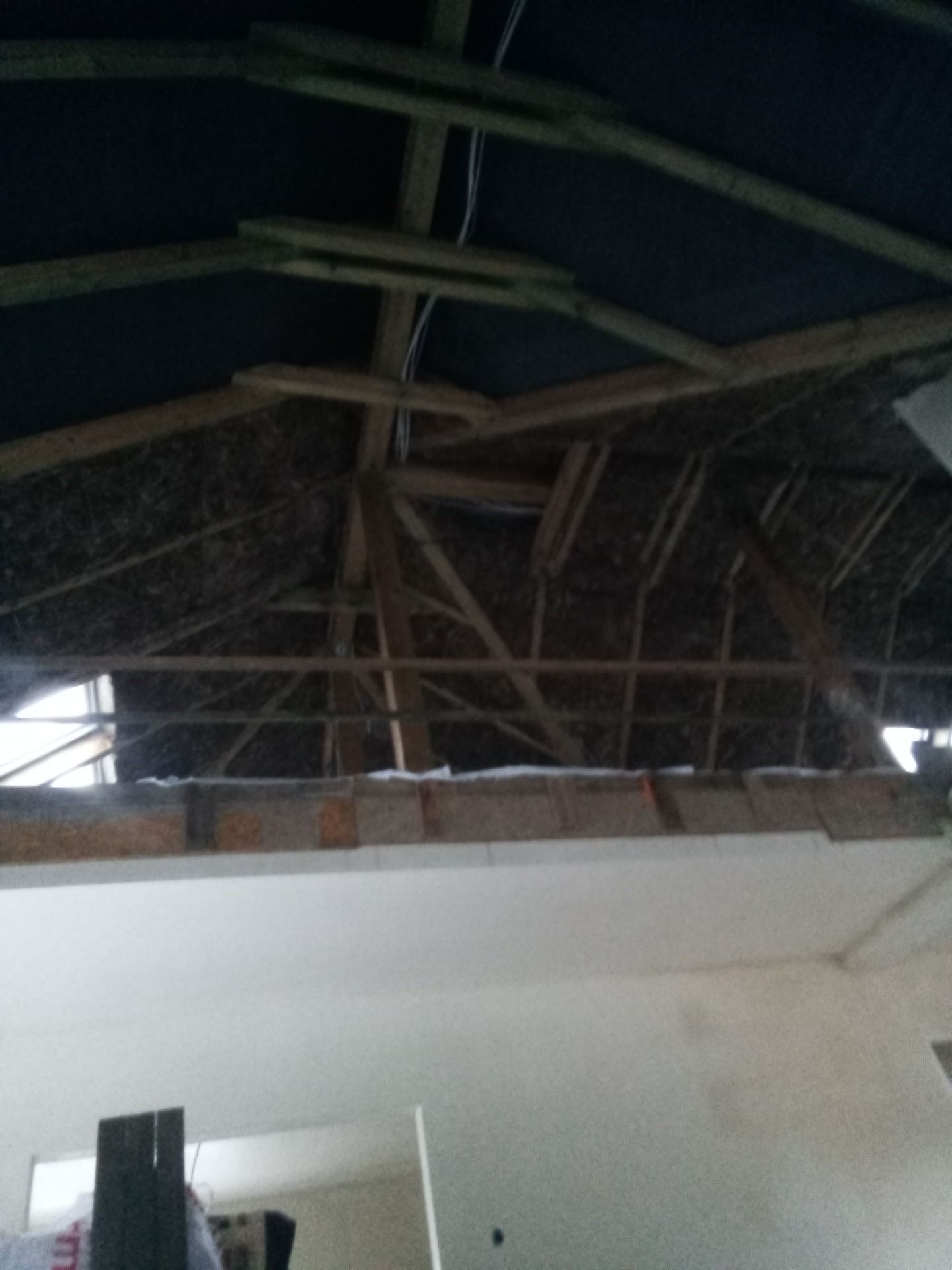 Wnętrze poddasza w trakcie ocieplania, widoczne krokwie, izolacja i fragment ściany.