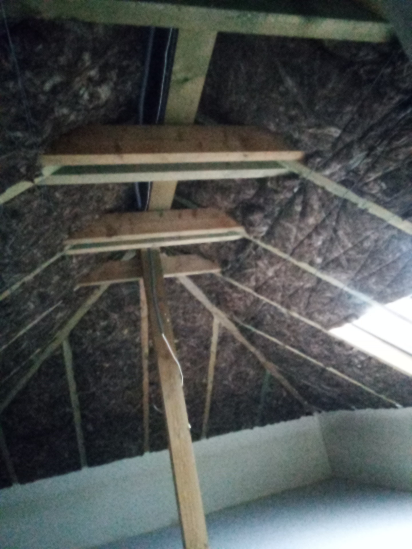 Skośne poddasze z widoczną drewnianą konstrukcją i izolacją z wełny mineralnej, fragment okna dachowego w tle, widok od dołu.