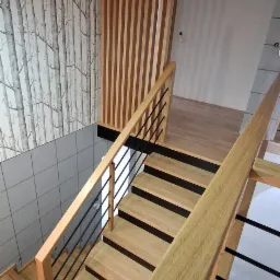 Nowoczesne schody o jasnym odcieniu drewna z czarnymi metalowymi elementami balustrady, widok z góry, z dekoracyjną ścianką z drewnianych listew i tapetą w motywie drzew.