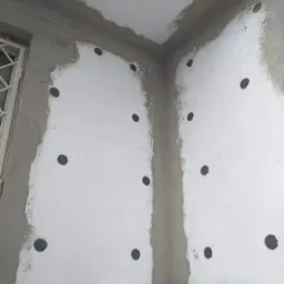 Fragment elewacji z zamocowanym styropianem, widoczne otwory na kołki, obok okno z kratą, na dole paczka styropianu Knauf.